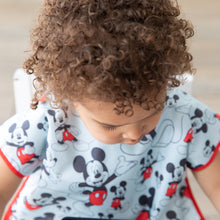 Load image into Gallery viewer, Close-up of a curly-haired child wearing a Bumkins Junior Bib: Mickey Mouse Classic looking down.
