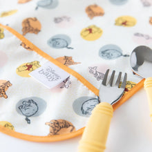 Load image into Gallery viewer, Close-up of a yellow fork and spoon lying on top of Bumkins Junior Bib: Winnie and Friends on a white background.
