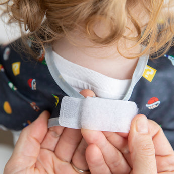 Hands fasten the hook-and-loop closure of a Bumkins Junior Bib: Super Mario™ Lineup around a child's neck.