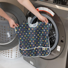 Load image into Gallery viewer, A person holds Bumkins Junior Bib: Super Mario™ Lineup in front of an open front-loading washing machine.
