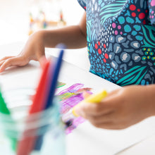 Load image into Gallery viewer, Close-up of a child in a Bumkins Short-Sleeved Smock: Animal Prints painting on paper; a jar of brushes is in the foreground.
