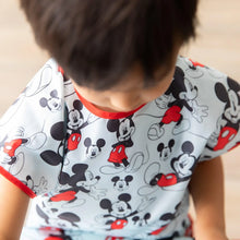 Load image into Gallery viewer, A child wearing a Bumkins Short-Sleeved Smock: Mickey Mouse Classic looking down.
