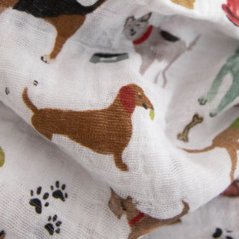 The Little Unicorn Cotton Swaddle Set, Woof, features breathable cotton muslin with colorful dog illustrations and paw prints.