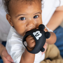 Load image into Gallery viewer, A curly-haired baby chews on a Bumkins Silicone Un-Droppable Mitt Teether: Mickey Mouse while sitting on an adult's lap.
