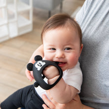 Load image into Gallery viewer, A baby chews on a Bumkins Silicone Un-Droppable Mitt Teether: Mickey Mouse, cradled by an adult.
