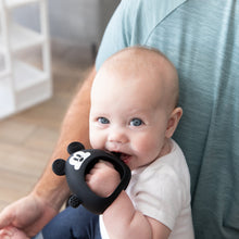Load image into Gallery viewer, A blue-eyed baby nibbles on a Bumkins Silicone Un-Droppable Mitt Teether: Mickey Mouse while sitting on someone's lap indoors.
