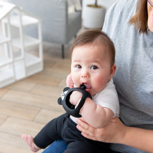 Load image into Gallery viewer, A baby sits on an adult's lap indoors, nibbling a Bumkins Silicone Un-Droppable Mitt Teether: Mickey Mouse.
