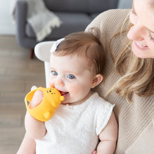 Load image into Gallery viewer, A baby with blue eyes chews a Bumkins Silicone Un-Droppable Mitt Teether: Winnie the Pooh, while held by a smiling woman in a beige sweater.
