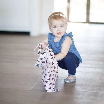 A toddler in a blue outfit crouches, holding a Bumkins Wet Bag: Hearts.