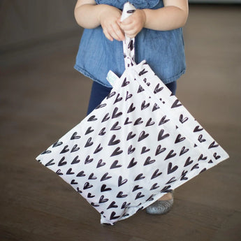 A child in blue holds a Bumkins Wet Bag: Hearts by the handle.