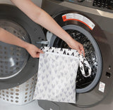 A person holds a Bumkins Wet Bag: Hearts in front of a front-loading washing machine.