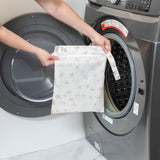 A person holds Bumkins Wet Bag: Palm Daze in front of an open front-loading washing machine.