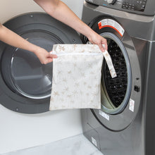 Load image into Gallery viewer, A person holds Bumkins Wet Bag: Palm Daze in front of an open front-loading washing machine.
