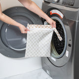 A person holds Roamio by Bumkins Wet Bag: Sand Check in front of an open front-loading washing machine.
