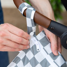 Load image into Gallery viewer, Close-up of a person attaching a Bumkins Wet Bag: Charcoal Check to a stroller handle using the snap button on the handle.
