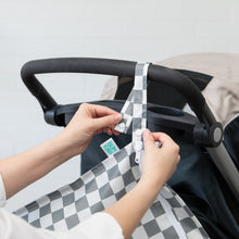 Load image into Gallery viewer, Hands attaching a Bumkins Wet Bag: Charcoal Check to a stroller handle.

