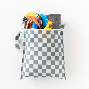 Bumkins Wet Bag: Charcoal Check holds flip-flops, a blue bottle, a toy dinosaur, and  a gray towel on a white background.