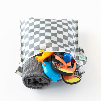 Bumkins Wet Bag: Charcoal Check is packed with a towel, toy dinosaur, flip-flops, and a blue water bottle peeking out on a white background.