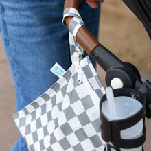 Load image into Gallery viewer, A Bumkins Wet Bag: Charcoal Check hangs on a stroller handle next to a cup holder with a drink.
