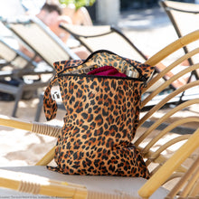 Load image into Gallery viewer, Roamio by Bumkins Wet Bag: Leopard rests on a rattan lounge chair outdoors, with clothes and a water bottle inside.
