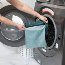 Load image into Gallery viewer, A person holds Bumkins Wet Bag: Starry Cactus in front of a front-loading washing machine.
