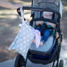 Load image into Gallery viewer, A baby sits in a stroller outdoors with a Bumkins Wet Bag: Arrow hanging from the handle, a purple cloth peeking out.
