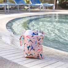 Load image into Gallery viewer, Bumkins Wet Bag: Yoga Pals holds a towel and water bottle poolside with empty lounge chairs in the background.
