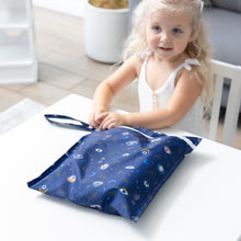 Load image into Gallery viewer, A child with blonde hair smiles at a table, holding Bumkins Wet Bag: Evil Eye.
