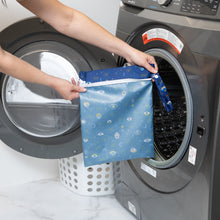 Load image into Gallery viewer, A person holds a Bumkins Wet Bag: Evil Eye in front of an open washing machine, with a white laundry basket in the background.
