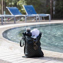 Load image into Gallery viewer, Roamio by Bumkins Wet Bag: Rich Black holds a towel, water bottle, and sunglasses poolside with empty blue lounge chairs behind.

