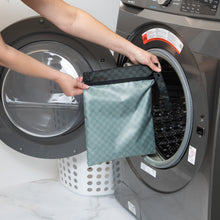 Load image into Gallery viewer, A person holds a Roamio by Bumkins Wet Bag: Rich Black in front of an open front-loading washing machine.
