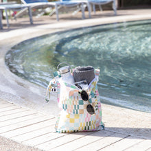 Load image into Gallery viewer, Roamio by Bumkins Wet Bag: Motley Check sits poolside, holding a towel, water bottle, camera, and sunglasses.
