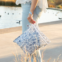 Load image into Gallery viewer, A woman stands on a concrete path by a pond with ducks, holding a Roamio by Bumkins Wet Bag: Shells.
