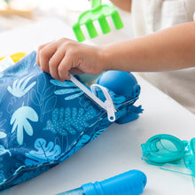 Load image into Gallery viewer, Close-up of a child's hand opening a Bumkins Wet Bag: Blue Tropic amid pool toys on a white table
