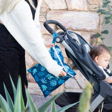 Load image into Gallery viewer, A person zips a Bumkins Wet Bag: Blue Tropic attached to a stroller with a child outdoors.
