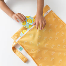Load image into Gallery viewer, Close-up of a child's hands tucking a colorful sandal into a Bumkins Wet Bag: Sunshine on a white table.
