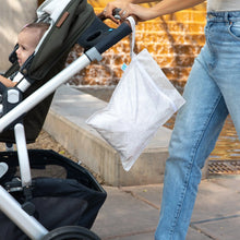 Load image into Gallery viewer, A person in jeans strolls by a fountain, pushing a stroller with a Bumkins Wet Bag: Wander hanging from the handle.
