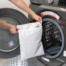 Load image into Gallery viewer, A person holds a Bumkins Wet Bag: Wander in front of an open front-loading washing machine.

