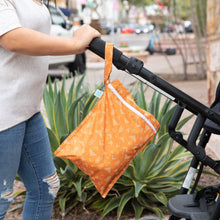 Load image into Gallery viewer, A person pushing a stroller with a Bumkins Wet Bag: Grounded attached to the handle, with plants and a street scene in the background.

