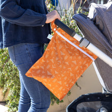 Load image into Gallery viewer, A person in jeans and a dark blue shirt pushes a stroller outdoors with a Bumkins Wet Bag: Grounded hanging from the handle.
