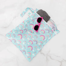 Load image into Gallery viewer, Bumkins Wet Bag: Rainbows holds a gray towel and pink sunglasses on a marble background.
