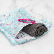Load image into Gallery viewer, Bumkins Wet Bag: Rainbows holds pink sunglasses, a rolled gray towel, and a book on a marble background.
