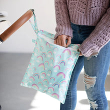 Load image into Gallery viewer, A person in a pink sweater and ripped jeans unzips a Bumkins Wet Bag: Rainbows hanging from a stroller handle.
