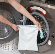 Load image into Gallery viewer, A person holds Bumkins Wet Bag: Rainbows in front of an open front-loading washing machine.
