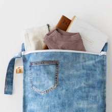 Load image into Gallery viewer, Roamio by Bumkins Wet Bag: Vintage Denim holds travel essentials like clothes, a passport, and notebook on a white background.
