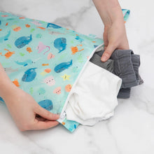Load image into Gallery viewer, Hands placing clothes into a Bumkins Wet Bag: Ocean Life on a marble surface.
