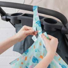 Load image into Gallery viewer, Hands attach a Bumkins Wet Bag: Ocean Life to a stroller handle using the snap button on the strap.
