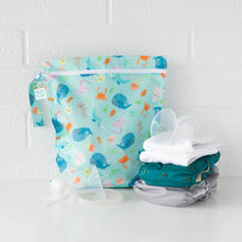 Load image into Gallery viewer, Bumkins Wet Bag: Ocean Life sits on a white table against a white brick wall, with cloth diapers and breast pump parts in front.
