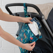Load image into Gallery viewer, A person places clothes into a Bumkins Wet Bag: Jungle, made of waterproof fabric, attached to a stroller handle.
