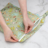 Hands zipping a Bumkins Wet Bag: Camp Gear, featuring trees and tents on waterproof fabric, on a marble surface.